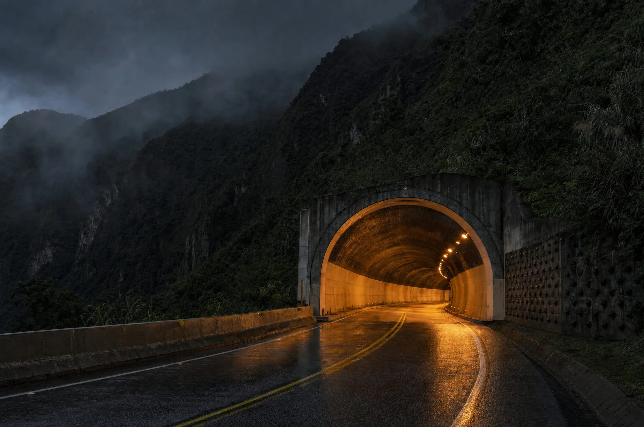 A mountain highway tunnel entrance lit by amber lights at night, evoking the Túnel de Oriente corridor between Medellín and Rionegro